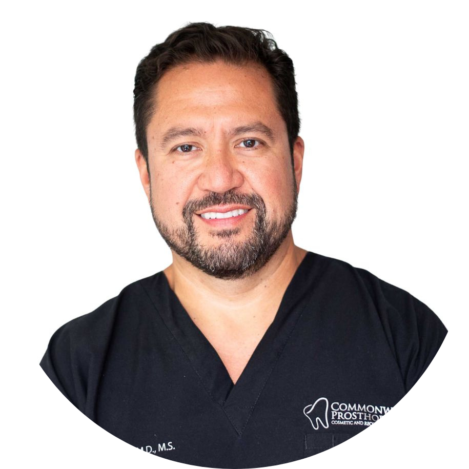 Headshot of a male dental professional wearing black scrubs, smiling against a white background.